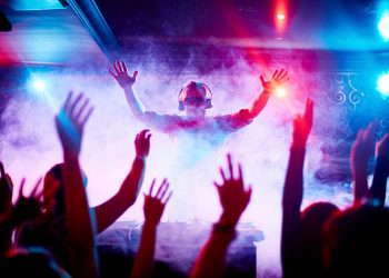 Male deejay in headphones and sunglasses looking at dancing crowd